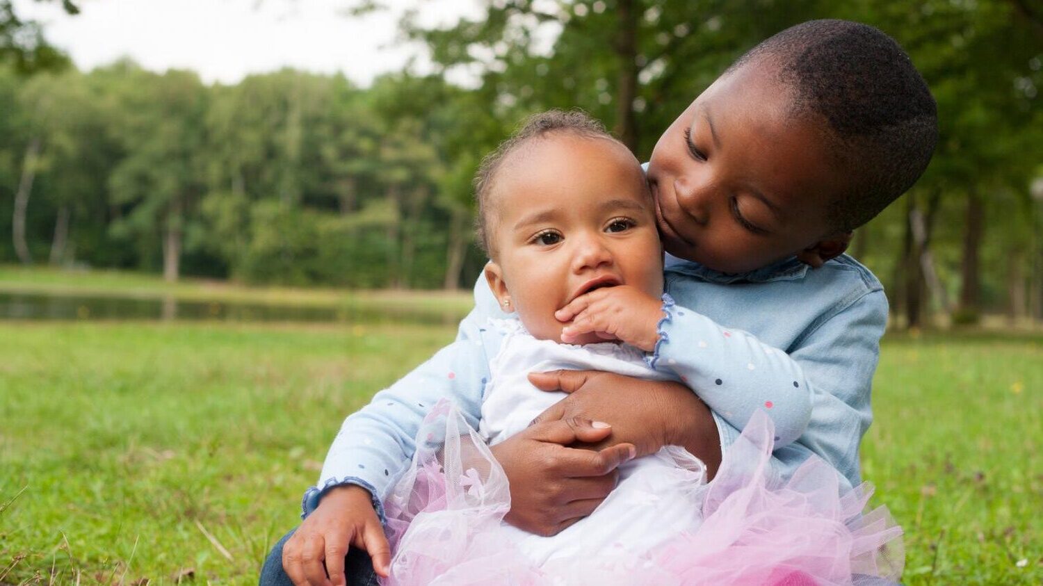 Two children sit in a grassy field