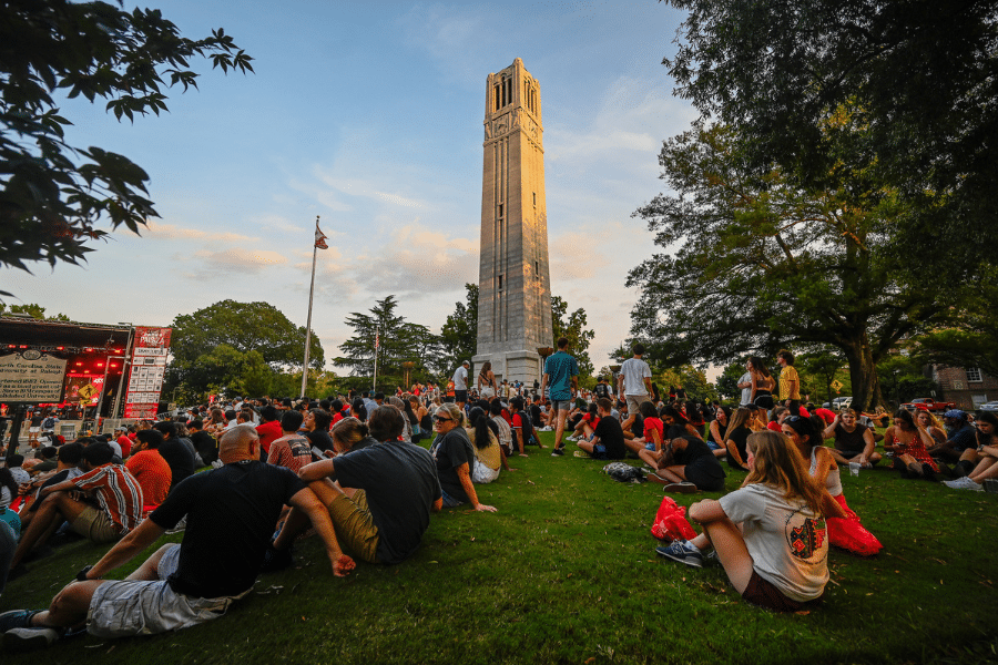 People are sitting together beside the bell tower at NC State